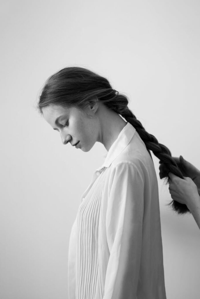 Black and white side profile of a woman having her hair braided by unidentifiable hands.