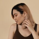 Portrait of an Asian woman with colored hair, eyes closed, posing against a beige background in a studio.